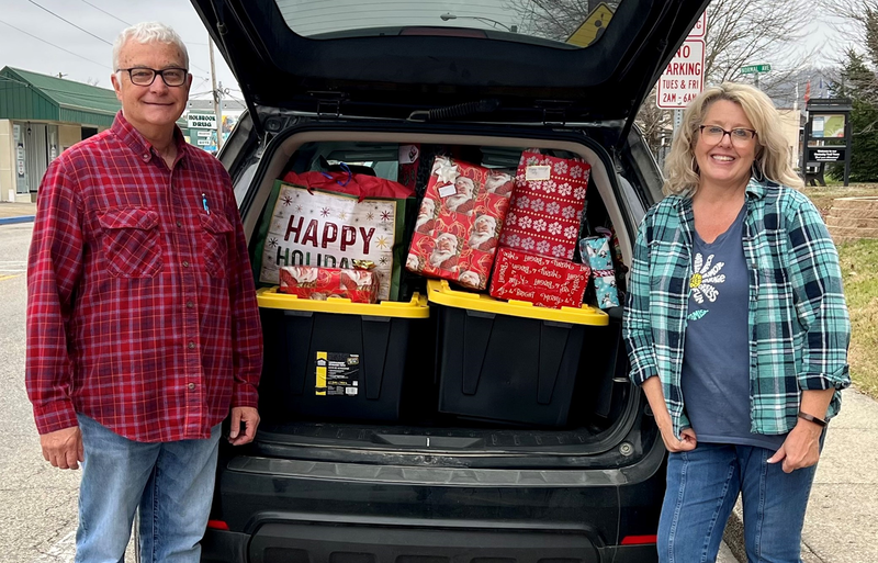 Man and woman standing next to vehicle filled with gifts.
