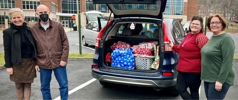 Four people next to vehicle filled with gifts.